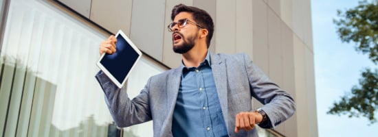 Man with a beard and glasses in a gray business suit running to work while grasping his tablet, as an example of ADHD in adults.