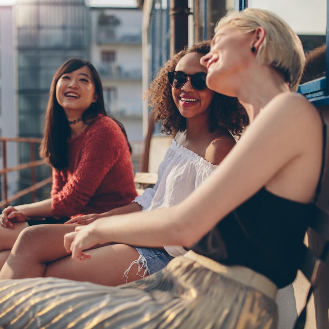 Three woman socializing on a balcony after one has gone to chronic illness and pain counseling.