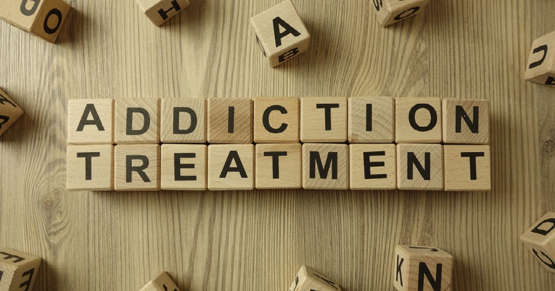 Scrabble tiles spell out ADDICTION TREATMENT on a wooden table. for online addiction treatment.