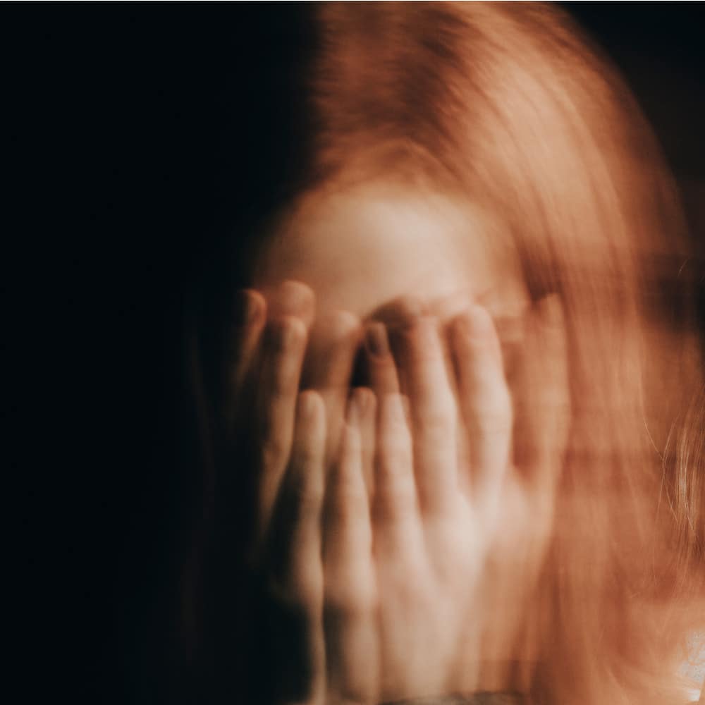 Blurry photo in the shape f a circle of a woman with ptsd and substance abuse disorder holding her hands over her face in need of online PTSD counseling.