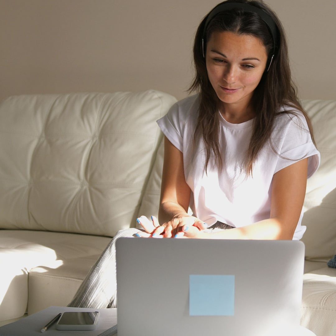 Woman with a laptop working with an online addiction therapist sitting on a white couch.