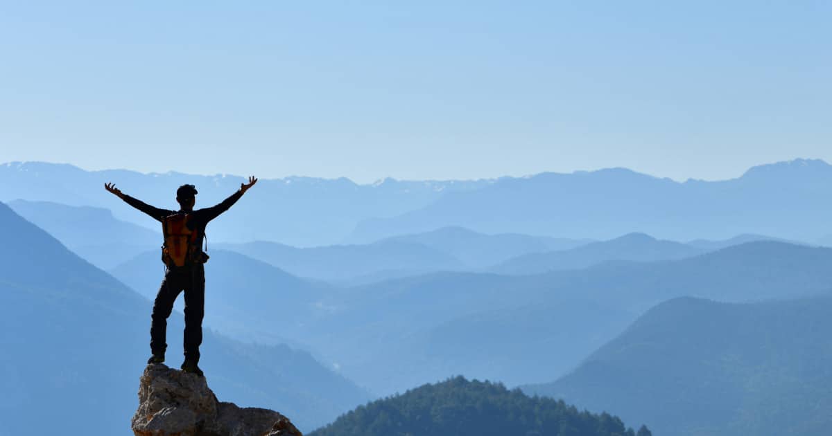 Man standing on a mountaintop with his arms stretched out asking questions for personal discovery.