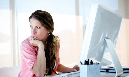 Distracted woman who needs adhd therapy online california sitting at her desk at work looking away from her computer daydreaming.