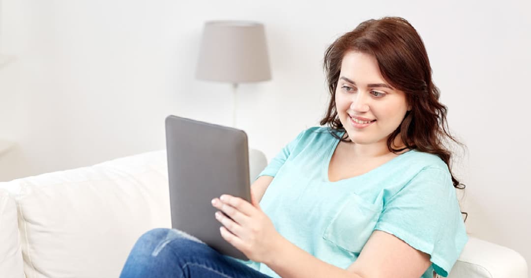 Woman wearing a light blue t-shirt holding a tablet while she smiles and participates in adult therapy services.