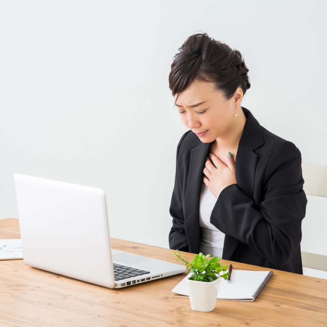 Asian woman with her hair up wearing a dark blazer at work taking a break to practice anxiety relief techniques.