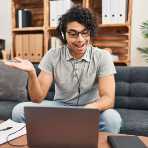 Young man with curly hair wearing a headset sitting on the couch with his laptop on a coffee table working with his anxiety therapist in california.