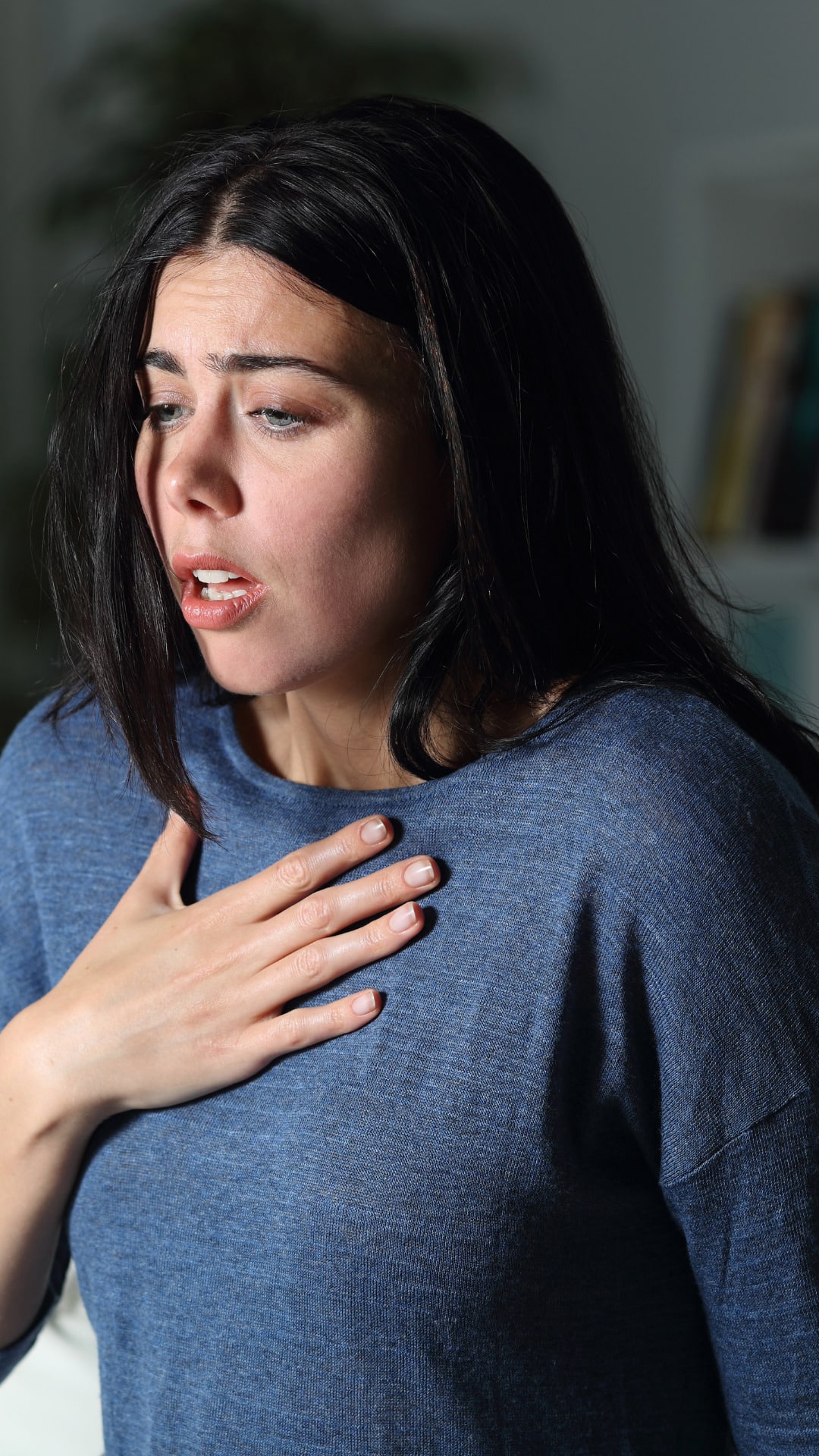 A woman with dark shoulder-length hair wearing a blue shirt with her hand on her chest having feelings of anxiety and thinking about anxiety therapy online in California for help.