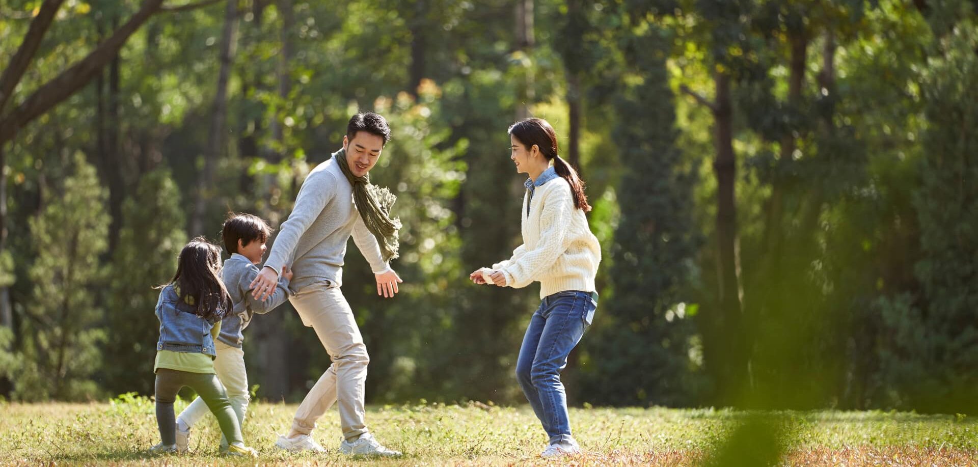 Asian parents demonstrating their authentic living principals playing with their kids in the park to support them in significant personal growth.