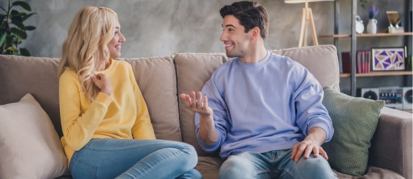 A young couple  smiling while sitting on the couch having a comfortable discussion about the benefits of premarital counseling.