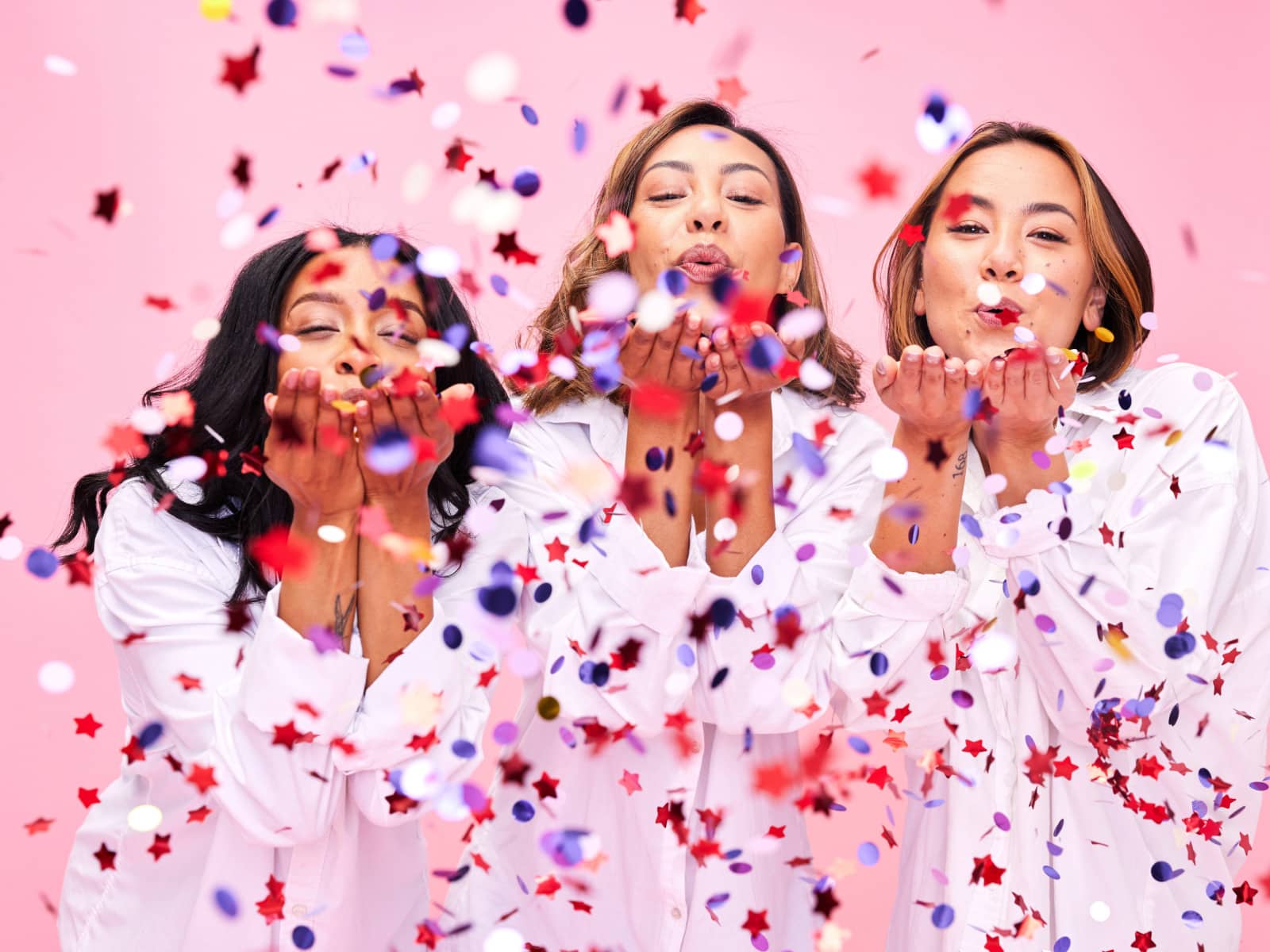 Three women dressed in white blowing confetti out of their hands to celebrate unique qualities,