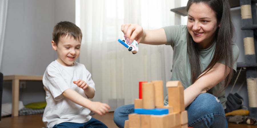 Mom playing blocks with her son. She's making a vehicle fly toward the blocks as her son shows his delight as a result of customized parenting sessions, her parent-child relationship has improved.