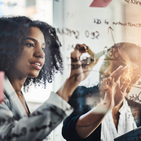 embrace new possibilities Two Black women dressed in suits working on a clear board together using math to embrace new possibilities.