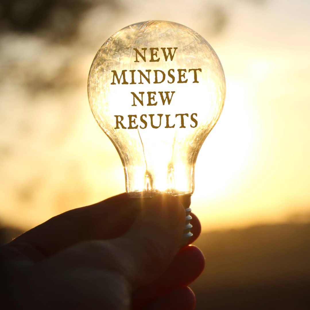 Someone holding a clear incandescent light bulb with the words "new mindset new results" to show they are embracing change positively.
