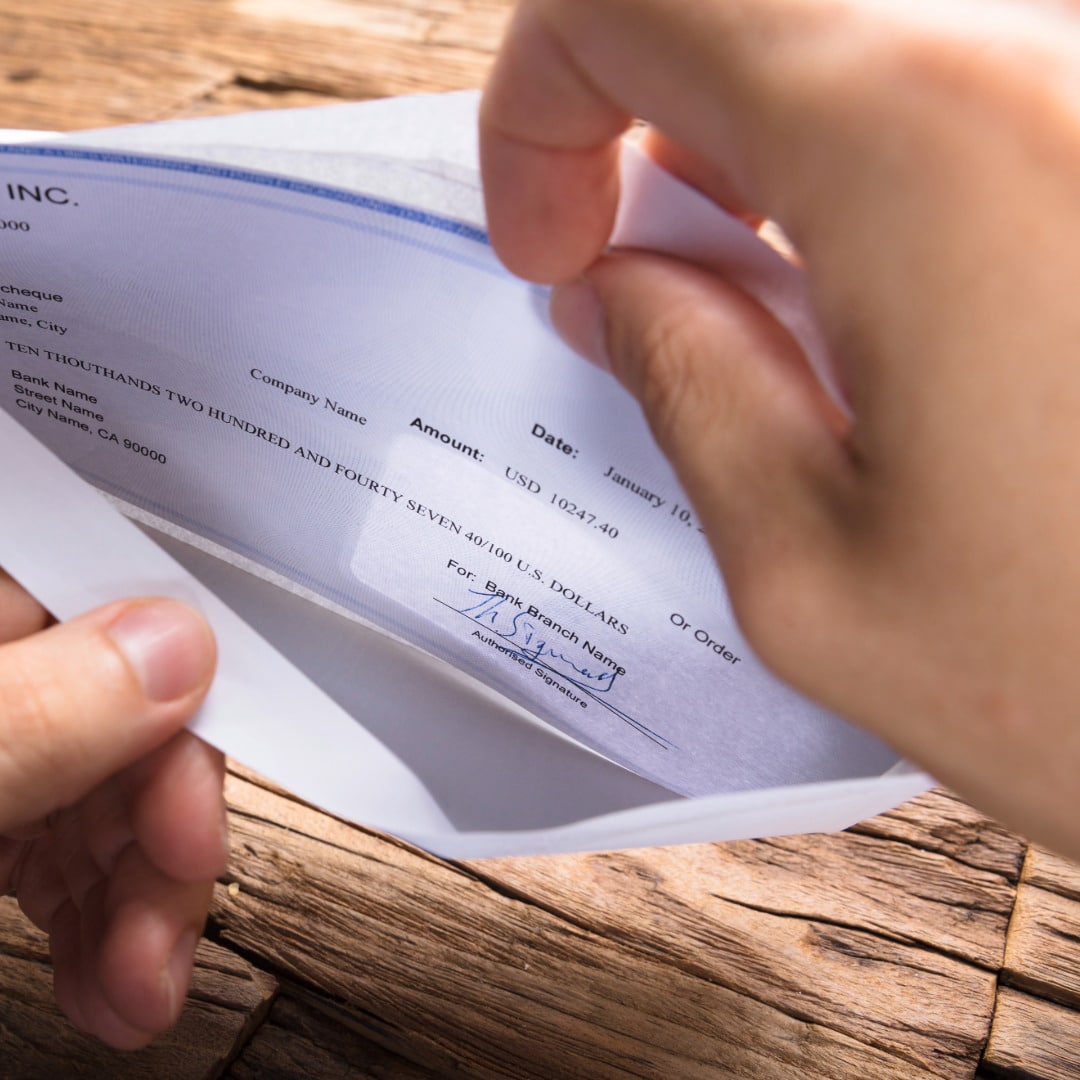 Hands opening a white envelope with a business check to get reimbursed for therapy.