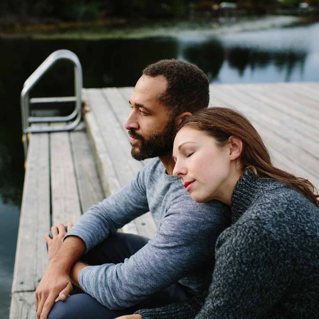 Couple sitting on a dock grieving the loss of their child before contacting a grief counselor for bereavement.