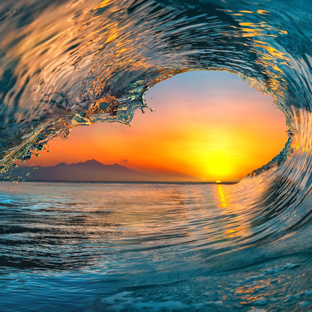 An ocean wave crashing down with an orange and yellow sunset showing through the center representing harm reduction for addiction as helpful building hope.