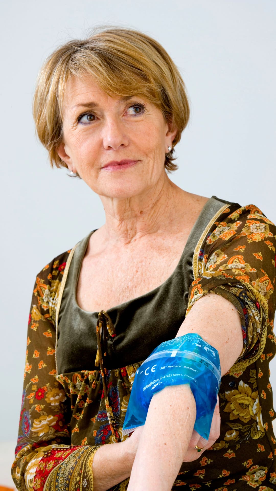 A middle age woman with short hair wearing a long sleeve top with one sleeve rolled up icing her elbow to help with pain from joint hypermobility. She is living with hypermobility and neurodiversity