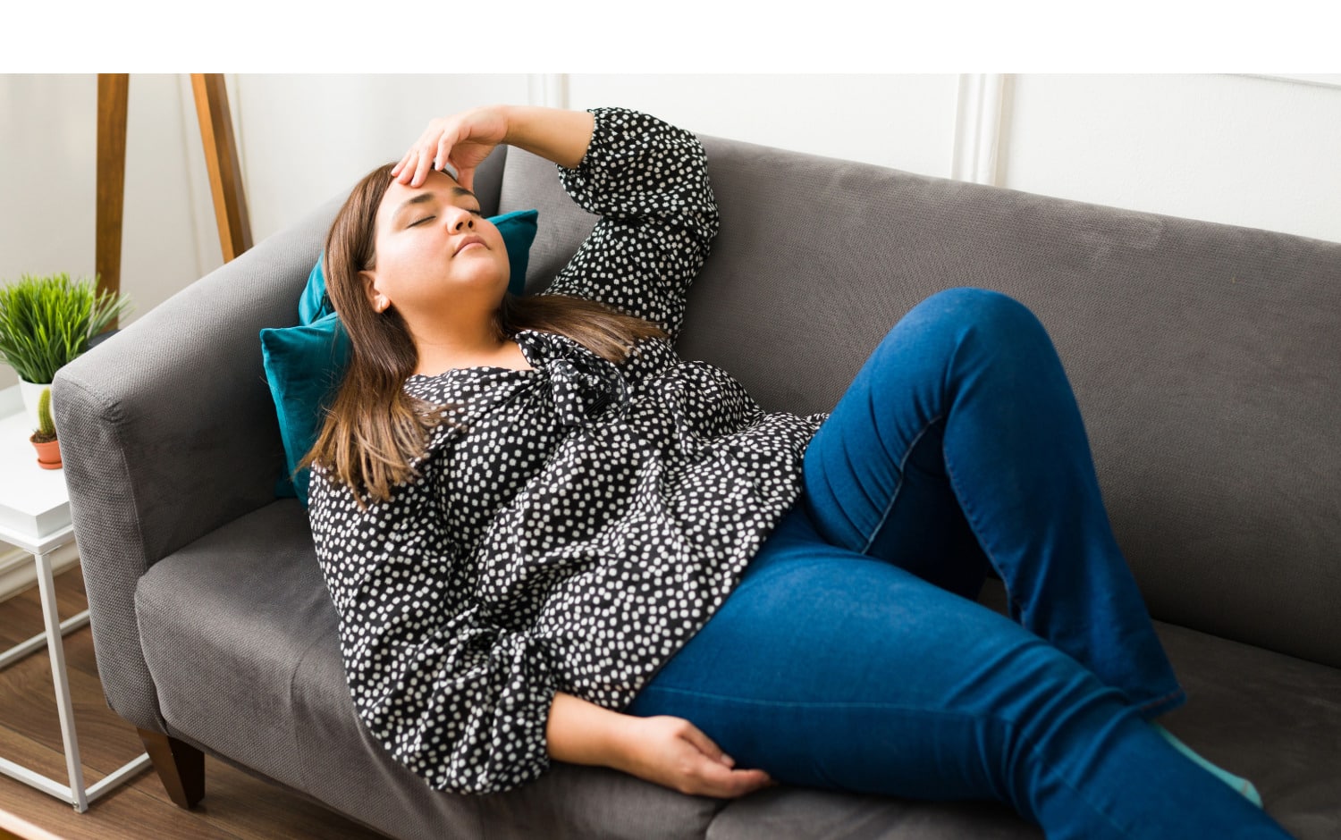 Woman with her hand on her forehead living  with hypermobility spectrum disorder taking time out to rest on the couch to preserve energy.