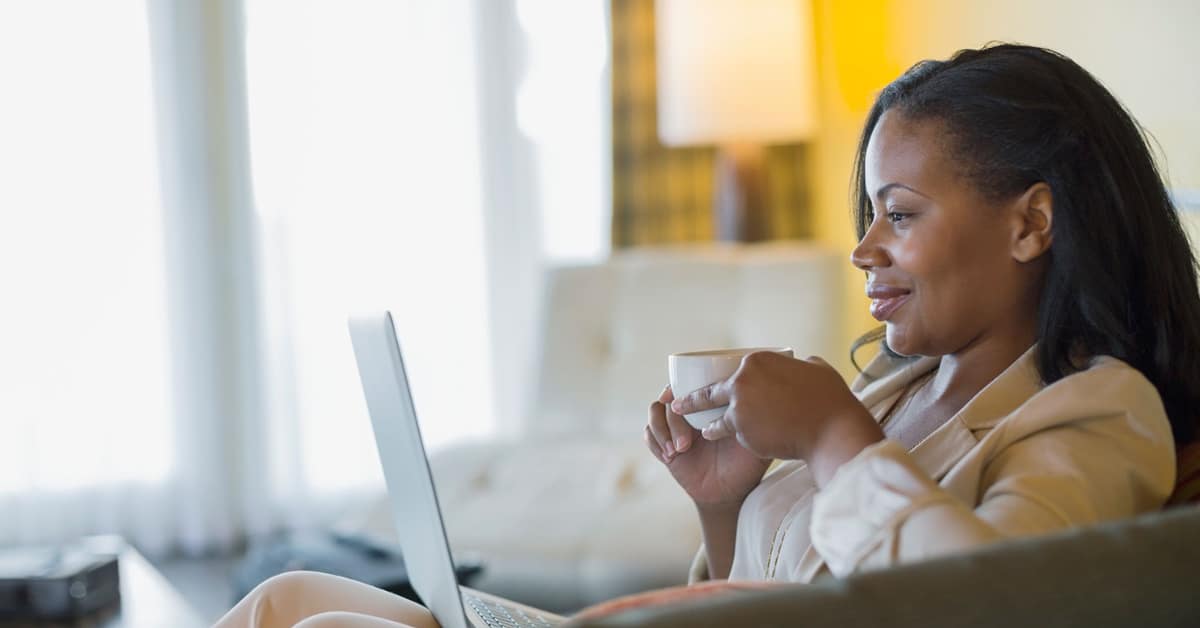 A Black woman sitting in her living room sipping tea as she works with her mental health therapist online california.