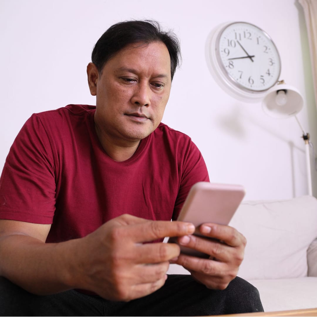 Man sitting the couch getting online ADHD treatment for adults on his smartphone.