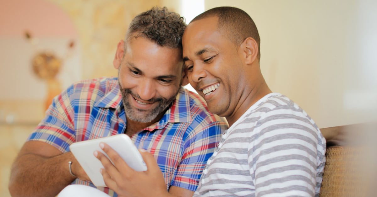 Gay men sitting together sharing a tablet for online relationship counseling.