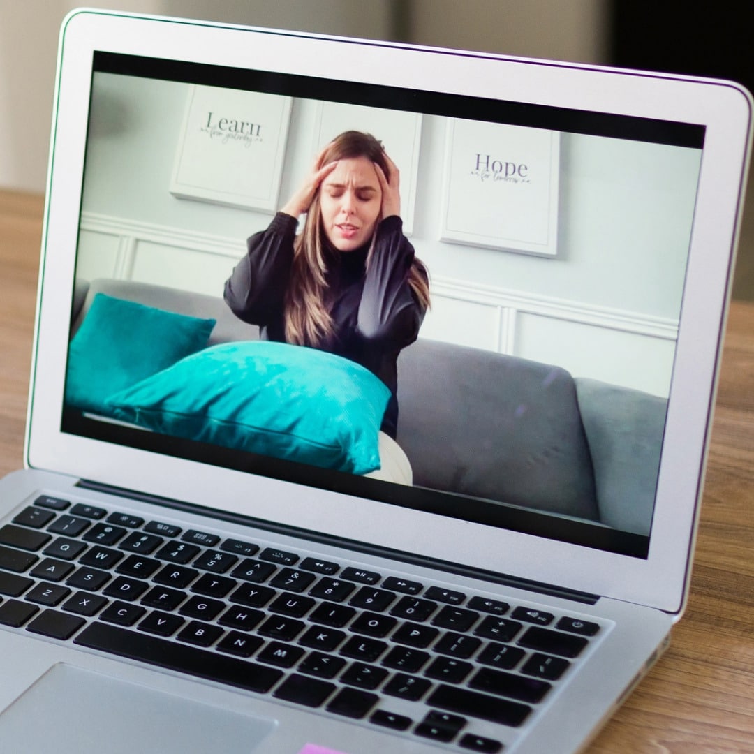 Photo of a client with long, straight hair with her eyes closed, holding her head with her elbows out able to express herself freely in the comfort of her own home because of her therapist's out-of-network provider decision.