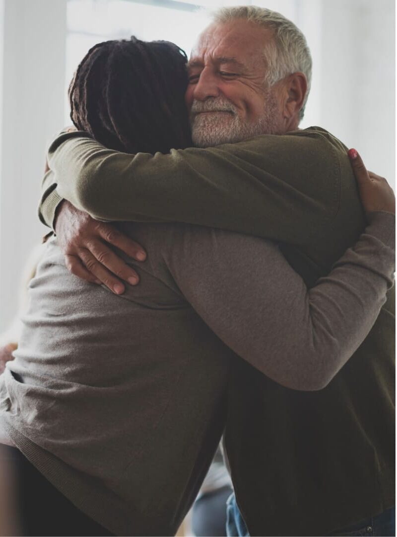 A man with gray hair and beard embracing a woman in support of her working on her solutions for PDA in adults.