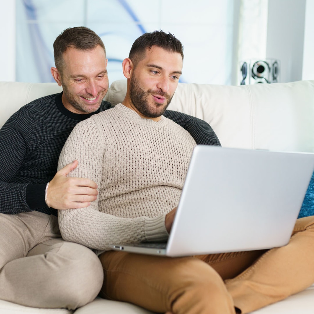 Gay couple sitting on the couch together with their laptop doing solution based treatment California for their relationship.
