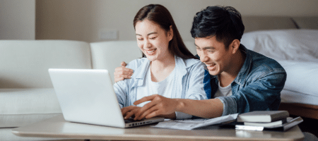 a casually dressed young Asian couple leaning in and sharing a white laptop to meet with their couple therapist for a session to work on solution focused approaches for relationship issues.