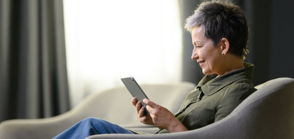 Woman with short greying hair sitting in a comfortable chair with her tablet working with a specialist for anxiety and depression.
