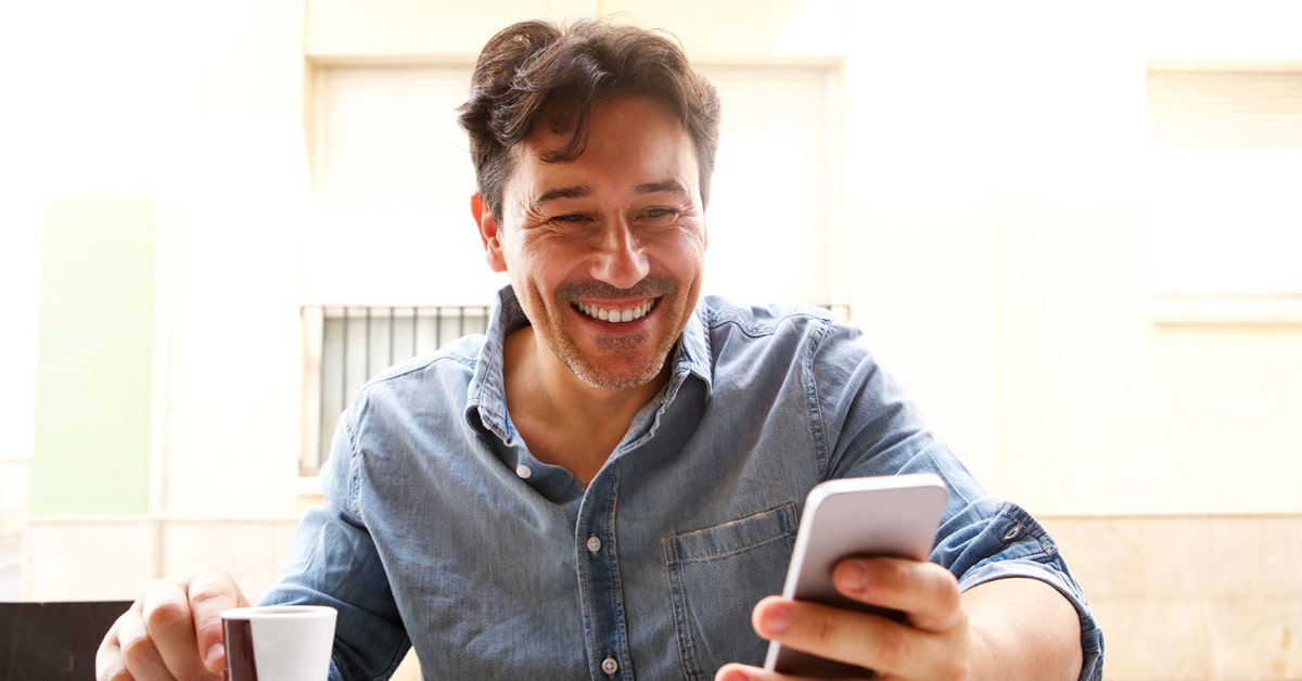 Man smiling while using his phone to meet with his therapist online therapy adult services.