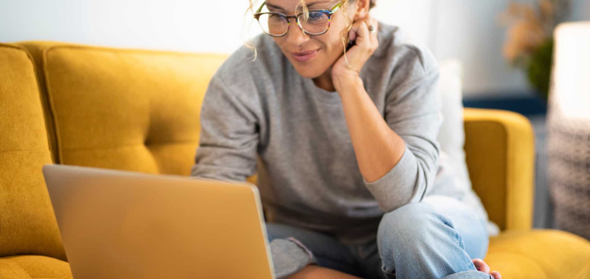 Black woman on a gold couch wearing gray sweats while getting trauma treatment online with a therapist.