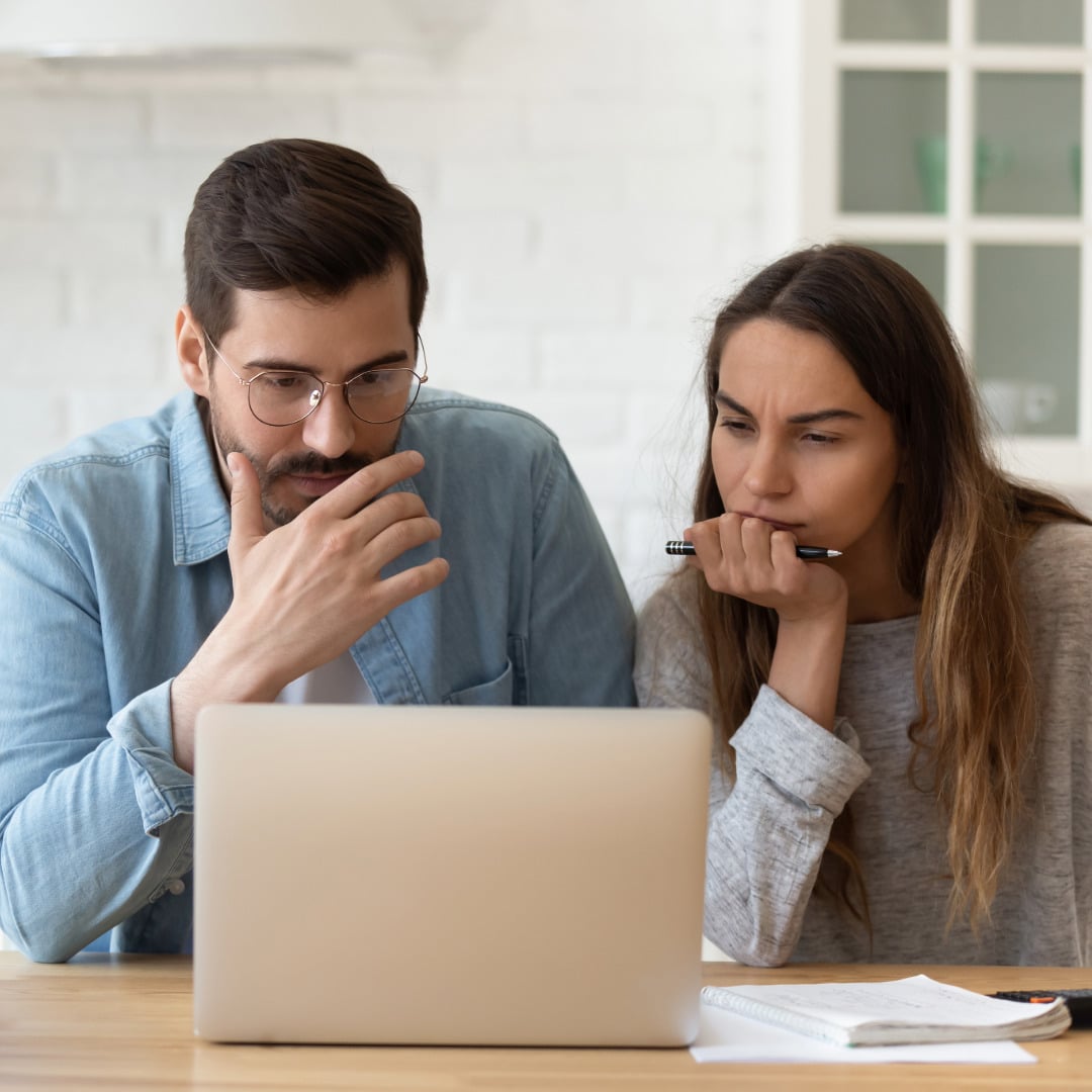 A couple in front of a laptop on a table. Both of them have their chin in their hand, focusing intently at the therapist on their screen during parenting counseling for unique parenting solutions to parenting challenges.