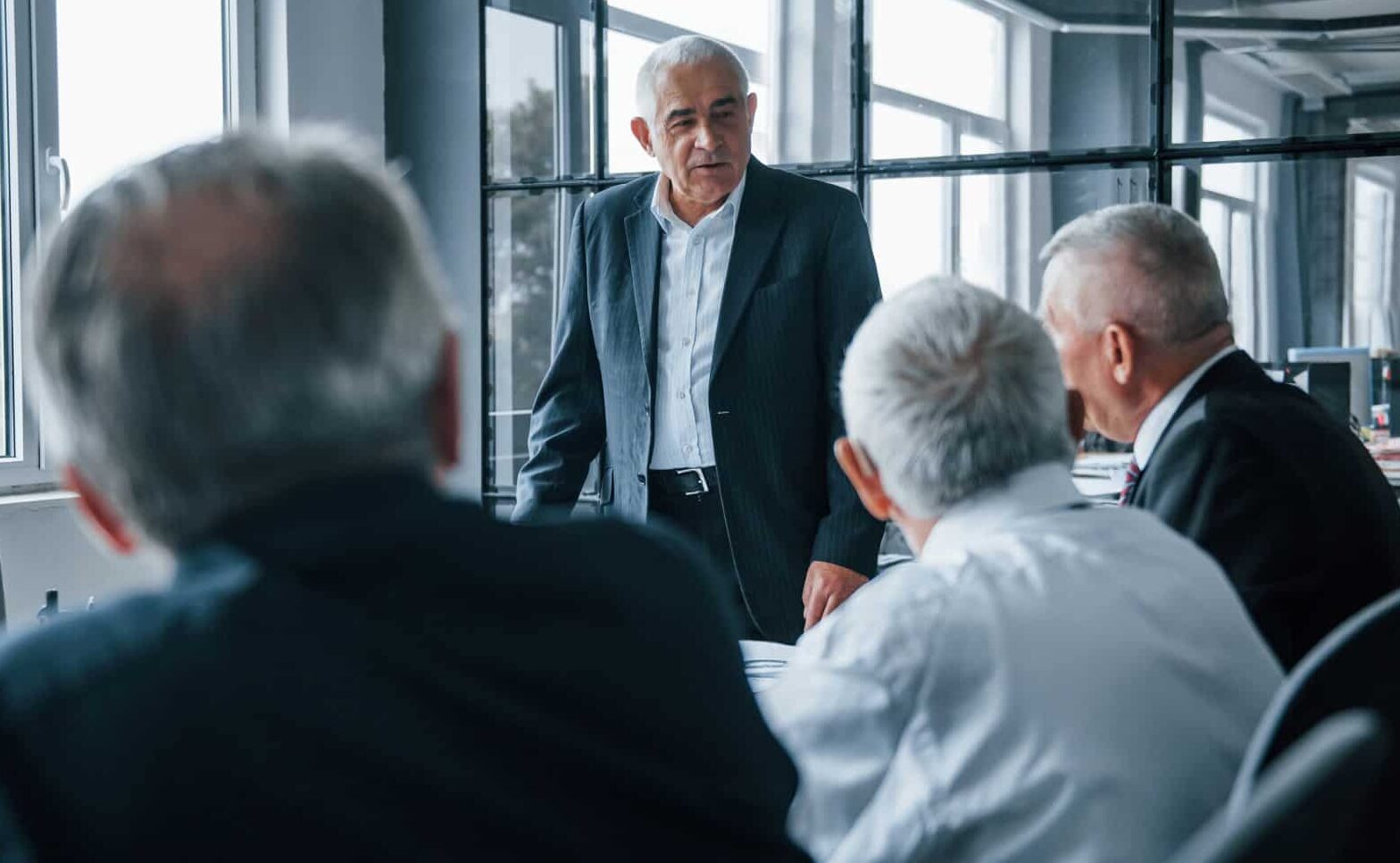 A group of older insurance executives with gray hair meeting around a conference table deciding on the rules for using your health insurance.