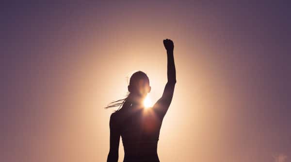 A silhouette of a woman with one arm up and the sunset shining over her shoulder showing her confidence after learning the answer to the question what is the foundation of therapy?